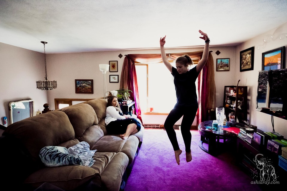 Mother watching teen daughter dance in living room with purple rug